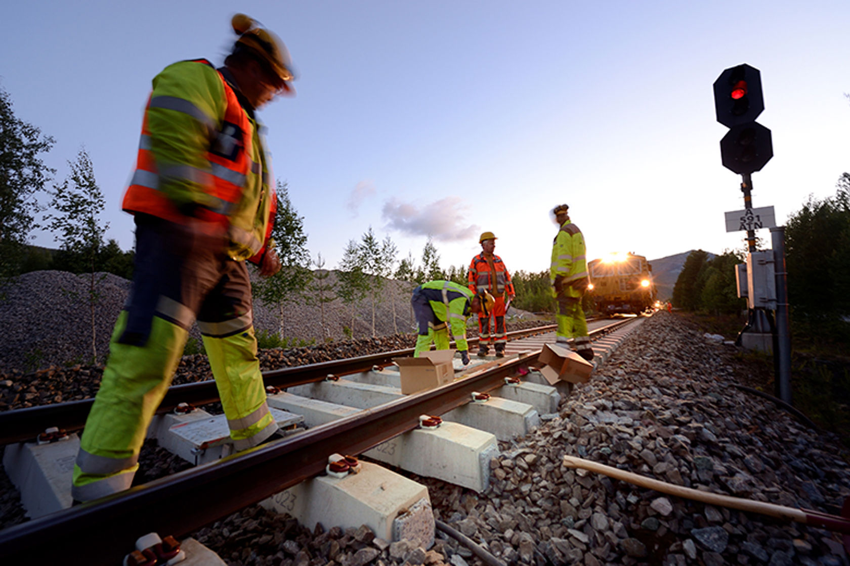 Tre mennesker i arbeidsklær står i bredbent i sporet. De er i gang med å bytte sviller. 