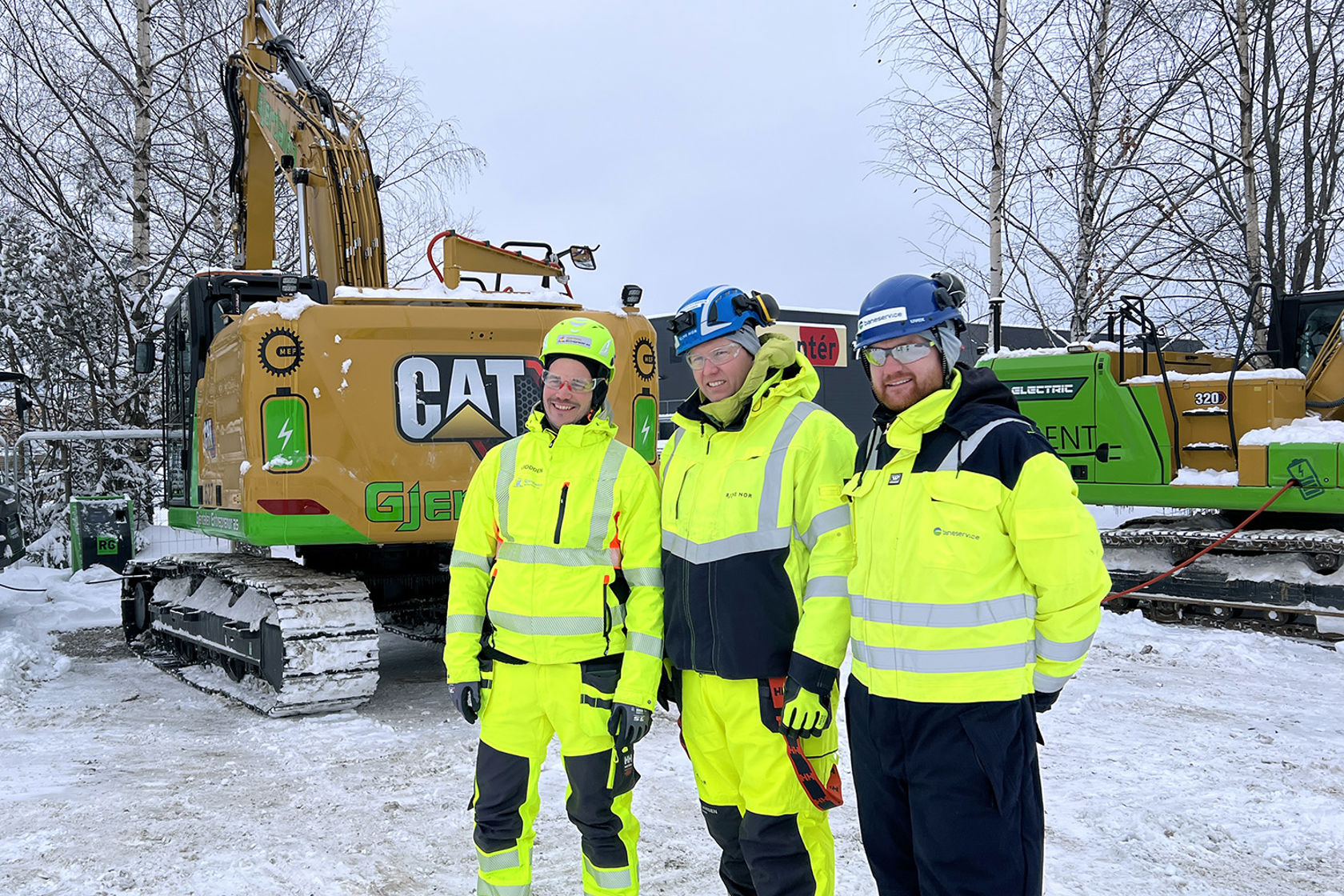 Personene i anleggsutstyr foran to gravemaskiner tilkoblet ladekabler. 