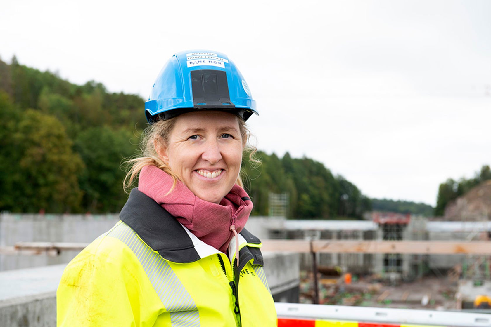 Portrett av Marianne med hjelm og vernetøy med anleggsarbeid i bakgrunnen.