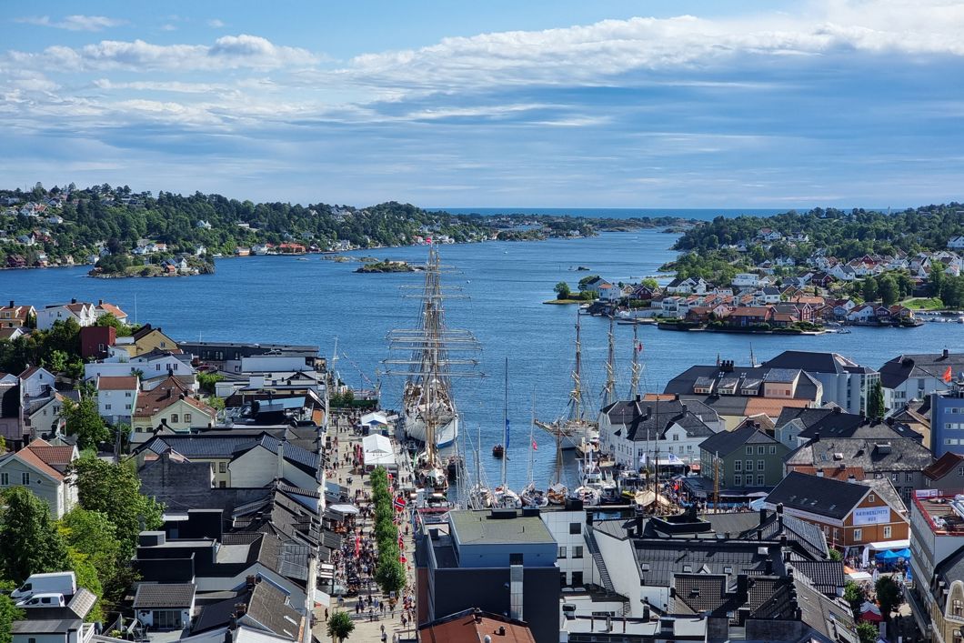 Oversiktsbilde over Arendal med hus, folk, bukt, seilskute og båter