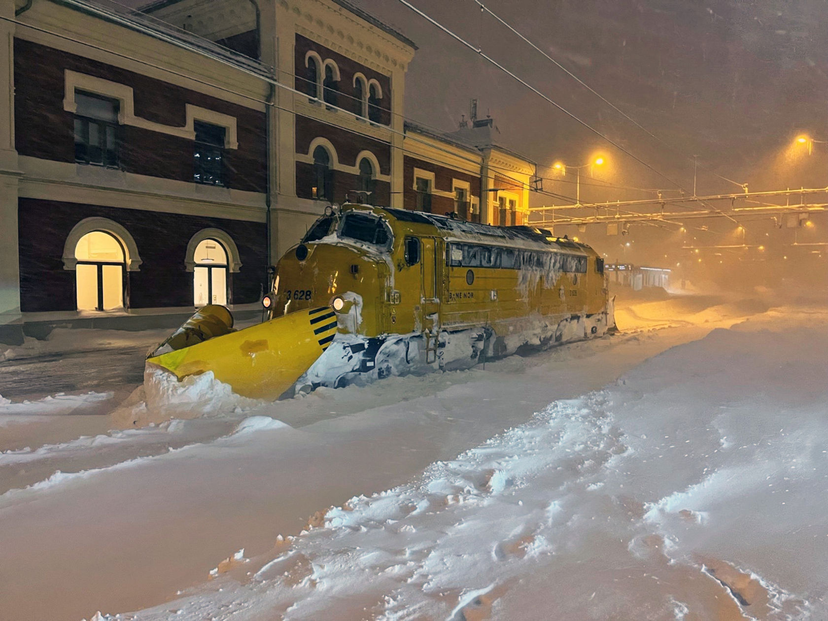 Arbeidstog med snøskuffe foran står parkert inne på en stasjon.