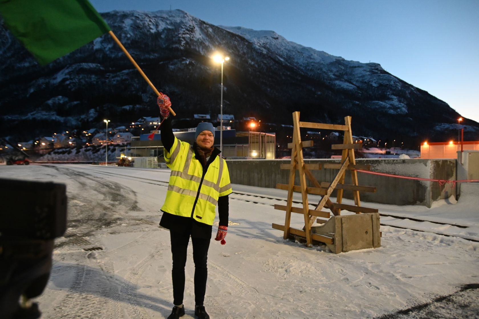 Mann i gul vest som veiver med et grønt flagg. 