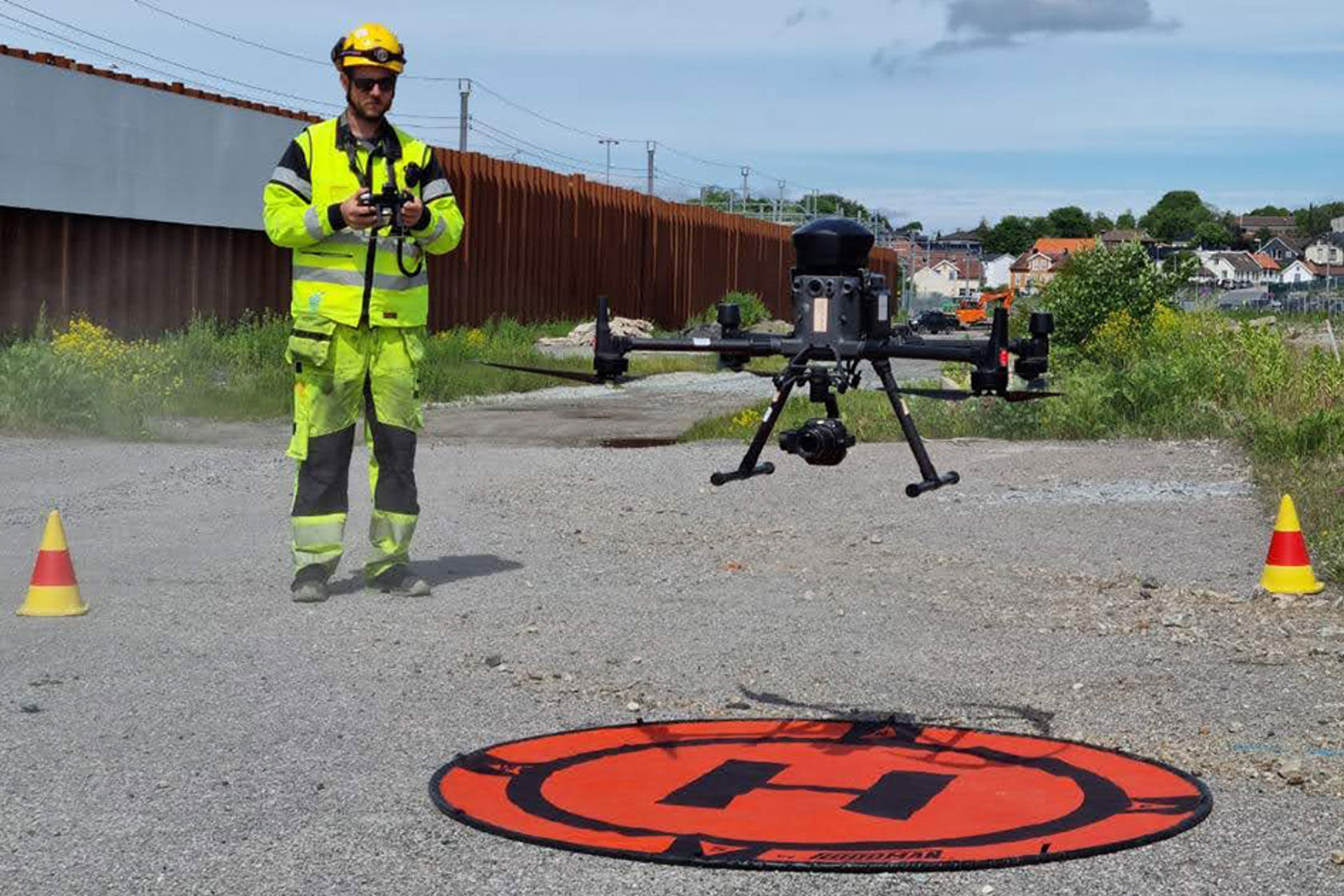 Mann i vernetøy holder i fjernkontroll. Foran sees drone som letter fra bakken.