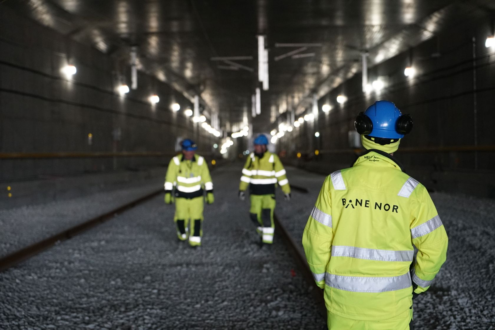 Folk i gult vernetøy går og befarer inne i en jernbanetunnel