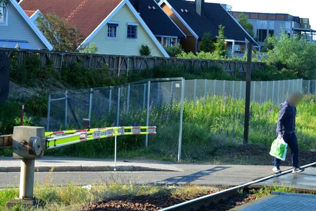 En person går over togets skinnegang mens bommen ligger nede.