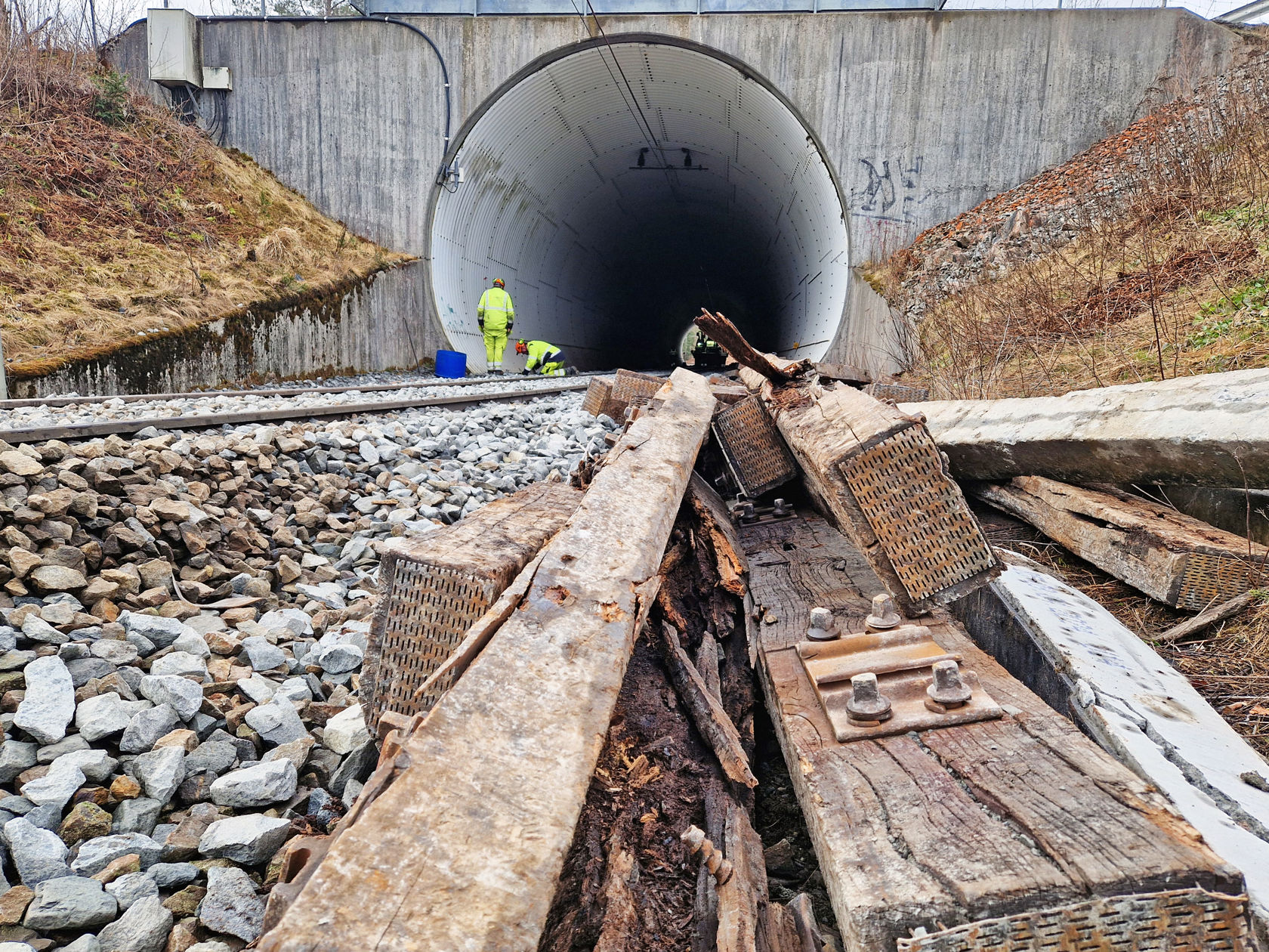 Noen gamle, råtne tresviller i forgrunn, jernbanespor som går inn i en tunnel i bakgrunn. 