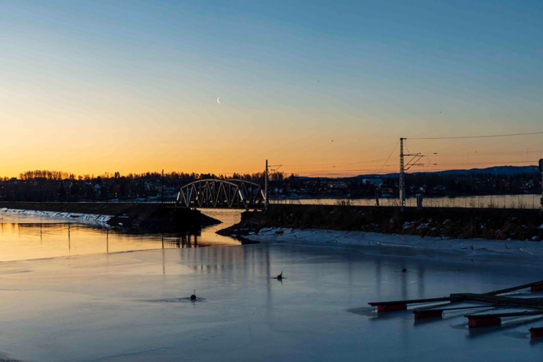 Solnedgang over en innsjø. Langs innsjøen går det jernbanespor. 